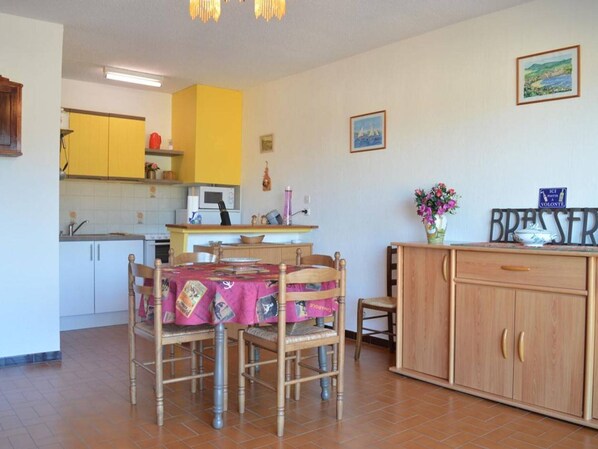 Cozinha compacta com armários amarelos, uma mesa de jantar com cadeiras e uma bancada pequena com pia.