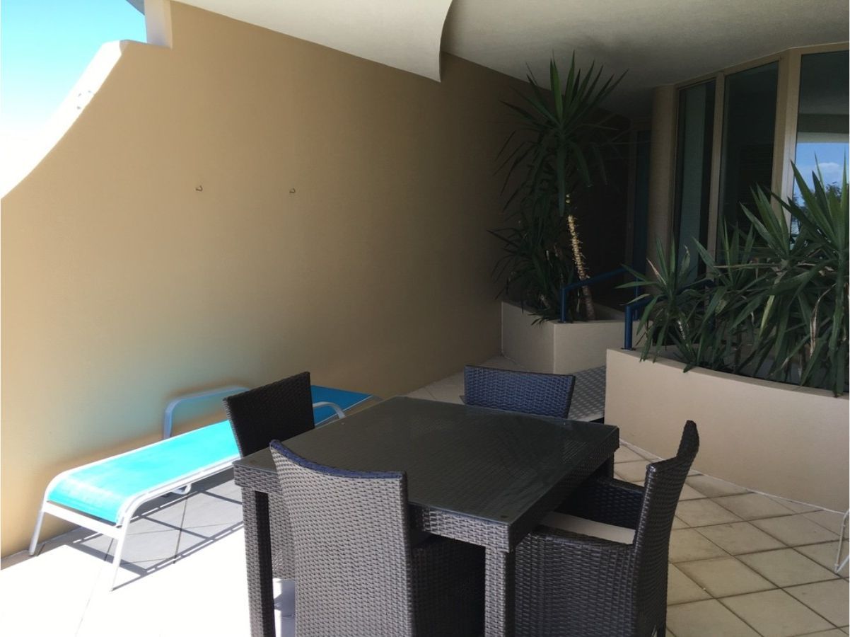 Un patio con mesa y sillas, una tumbona y plantas en macetas.