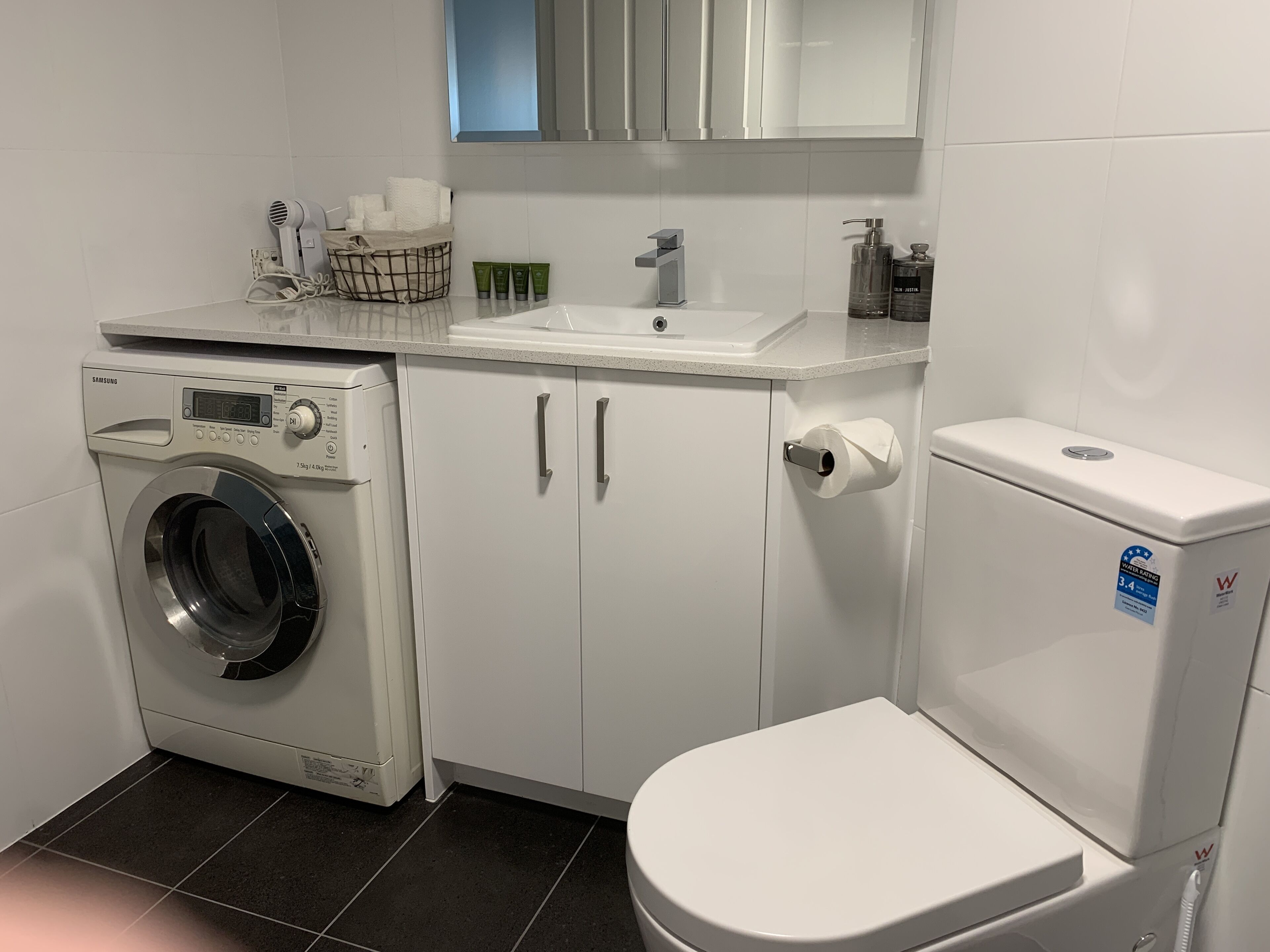 A compact bathroom with a washing machine, a toilet, and a sink.