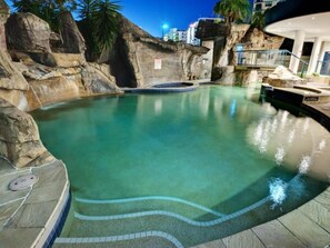 A swimming pool with clear water, surrounded by rock formations and palm trees. - Holiday With A View Landmark Hotel (Mooloolaba)
