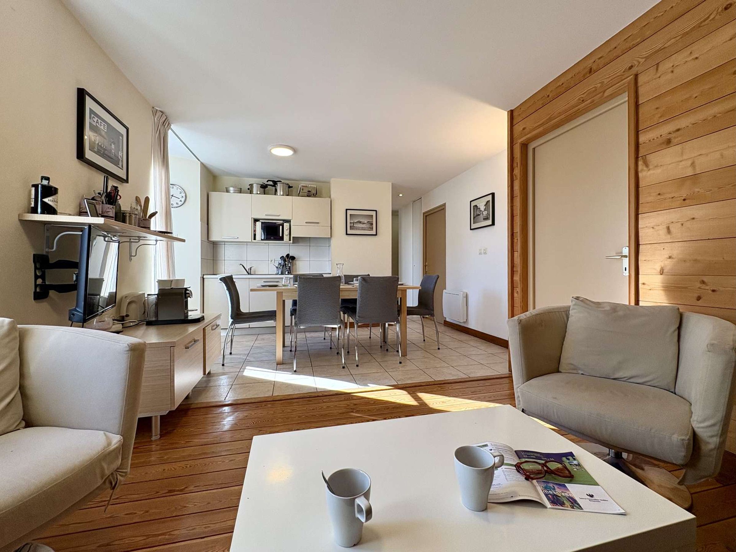 A modern living room with a sofa, a coffee table with two mugs, and a dining area with a table and chairs.