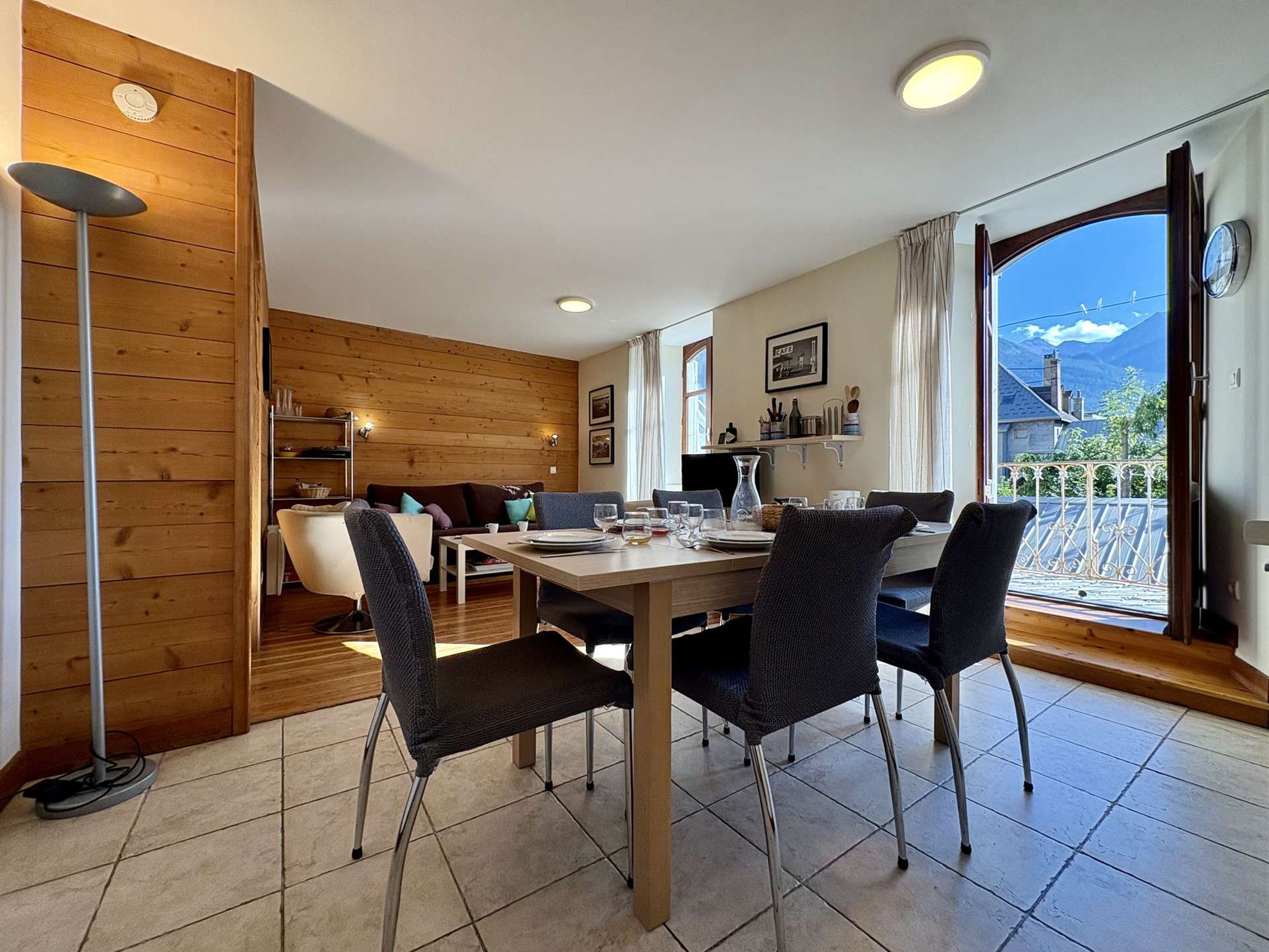 A dining area with a wooden table and chairs, a sofa, and a view of mountains through a large window.