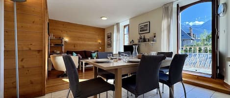 A dining area with a wooden table and chairs, a sofa, and a view of mountains through a large window.