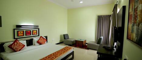 A hotel room with a bed, a desk, a chair, a ceiling fan, and artwork on the wall.