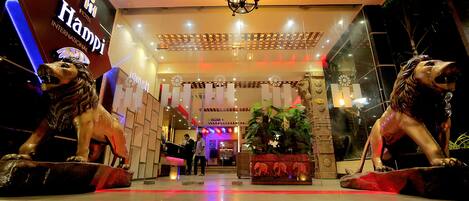 A hotel entrance with a sign reading "Hampi Hotel International," a chandelier, and two lion statues.