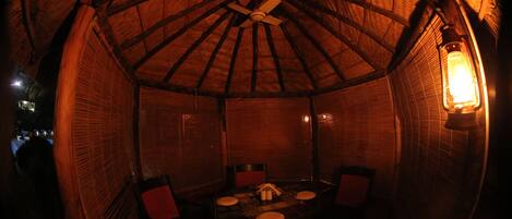 Una habitación circular con techo de madera y un ventilador central. Hay una mesa con sillas y un farol en la pared.