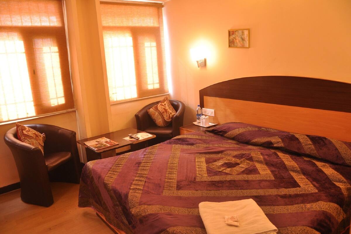 A hotel room with a large bed, a chair, a small table, and a wall-mounted lamp.