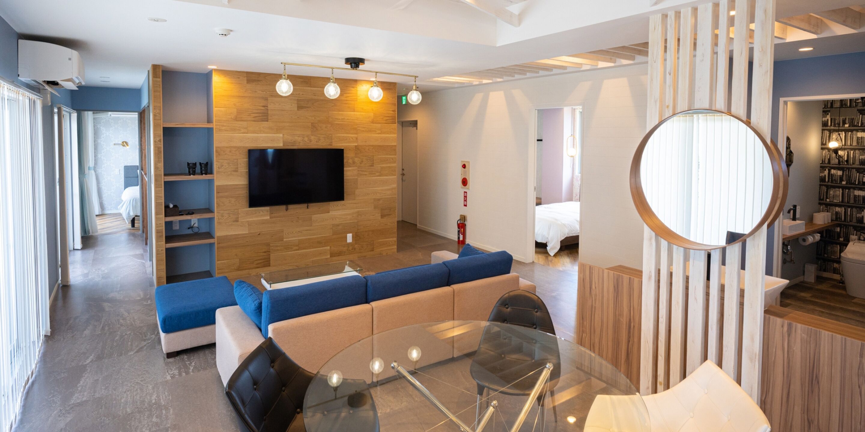 A modern living room with a large flat-screen TV, a glass coffee table, and a seating area with sofas and chairs.