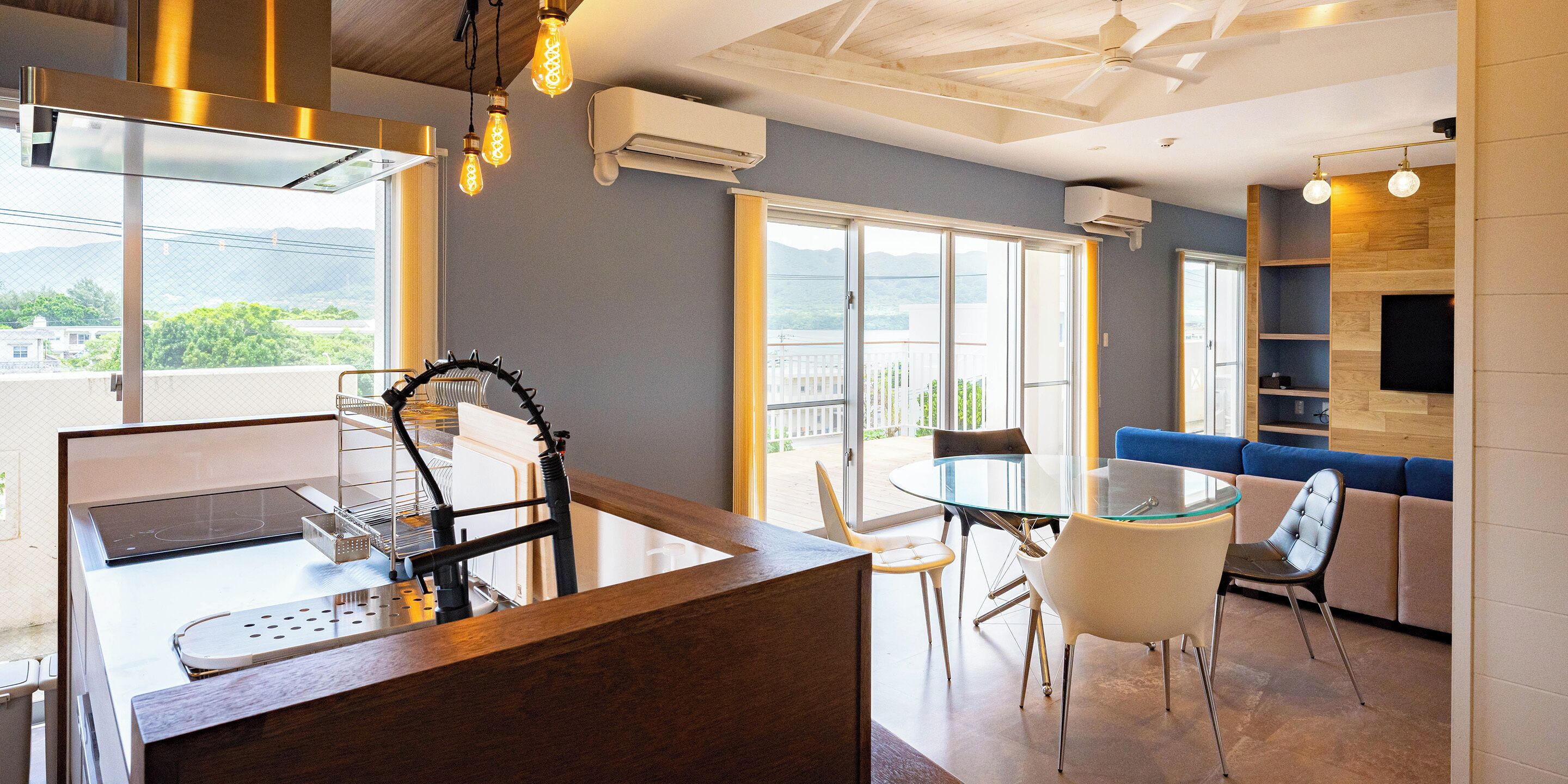 Una cucina moderna con isola in vetro, zona pranzo con tavolo e sedie in vetro e un angolo salotto con divano blu.