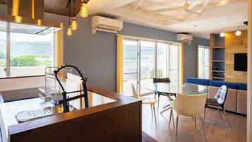 Una cucina moderna con isola in vetro, zona pranzo con tavolo e sedie in vetro e un angolo salotto con divano blu.
