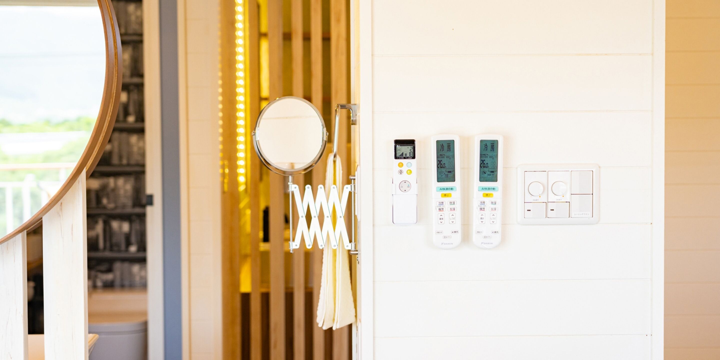 A bathroom with a mirror, towel rack, and two control panels on the wall.