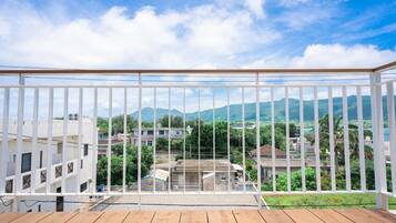 Ein Balkon mit Holzboden und weißen Geländern, mit Blick auf ein Wohngebiet mit Häusern und Bergen im Hintergrund.