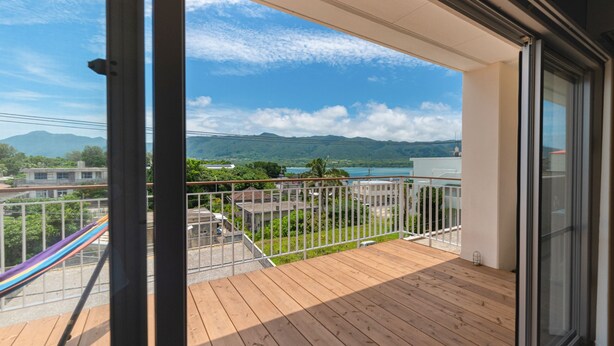Ein Balkon mit Holzboden, weißer Brüstung und Blick auf einen See und Berge.