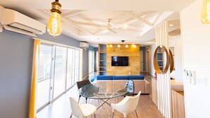 Ein modernes Interieur mit einem Glastisch, weißen Stühlen, einem blauen Sofa und einem an einer Holzwand befestigten Flachbildfernseher.