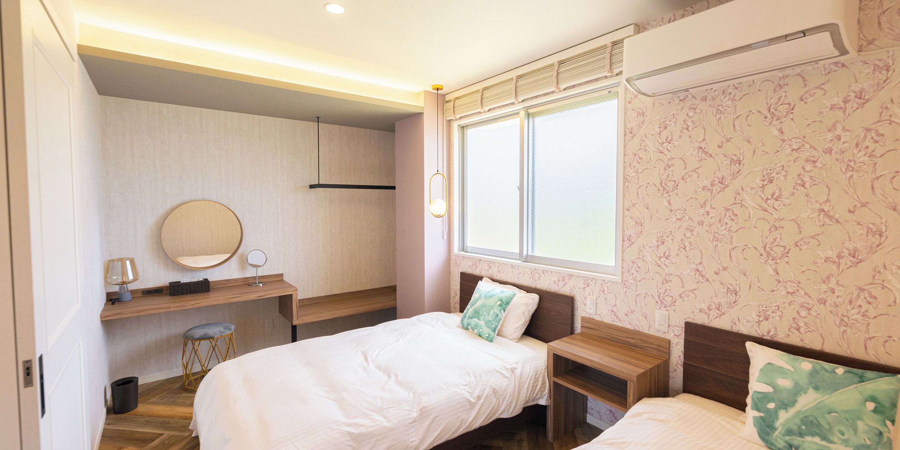A bedroom with two beds, a desk, a chair, a mirror, and a window.