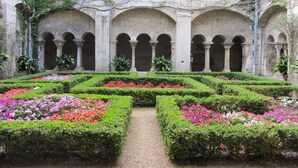 Un patio con un sendero central bordeado por macizos de flores simétricos y arcos.