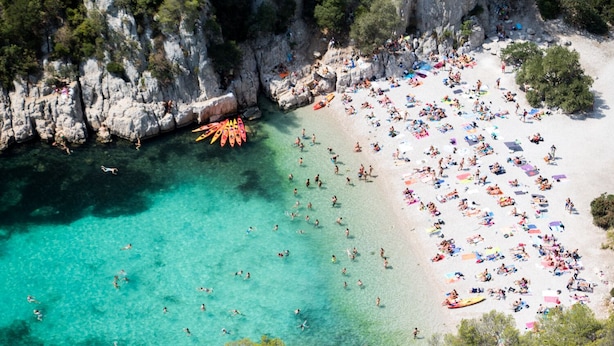 Una playa con agua turquesa cristalina, acantilados rocosos y numerosos kayaks.