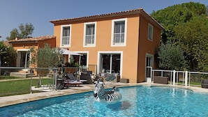 Una piscina con un flotador con estampado de cebra, rodeada por una casa con techo de tejas y ventanas amplias.