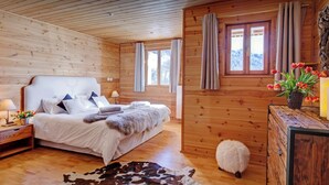 Un dormitorio de cabaña de madera con una cama grande, un aparador de madera, un tapiz de cuero de vaca y una oveja blanca pequeña.