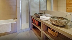 Un baño moderno con bañera, dos lavamanos, cabina de ducha de vidrio y estanterías de madera con cestas.