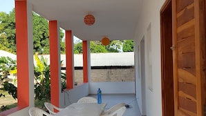 A covered patio area with a table and chairs, a wooden door, and a view of greenery outside.