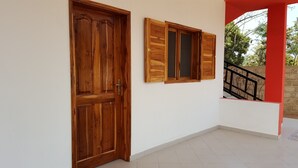A wooden door and a window with shutters, a tiled floor, and a red pillar.