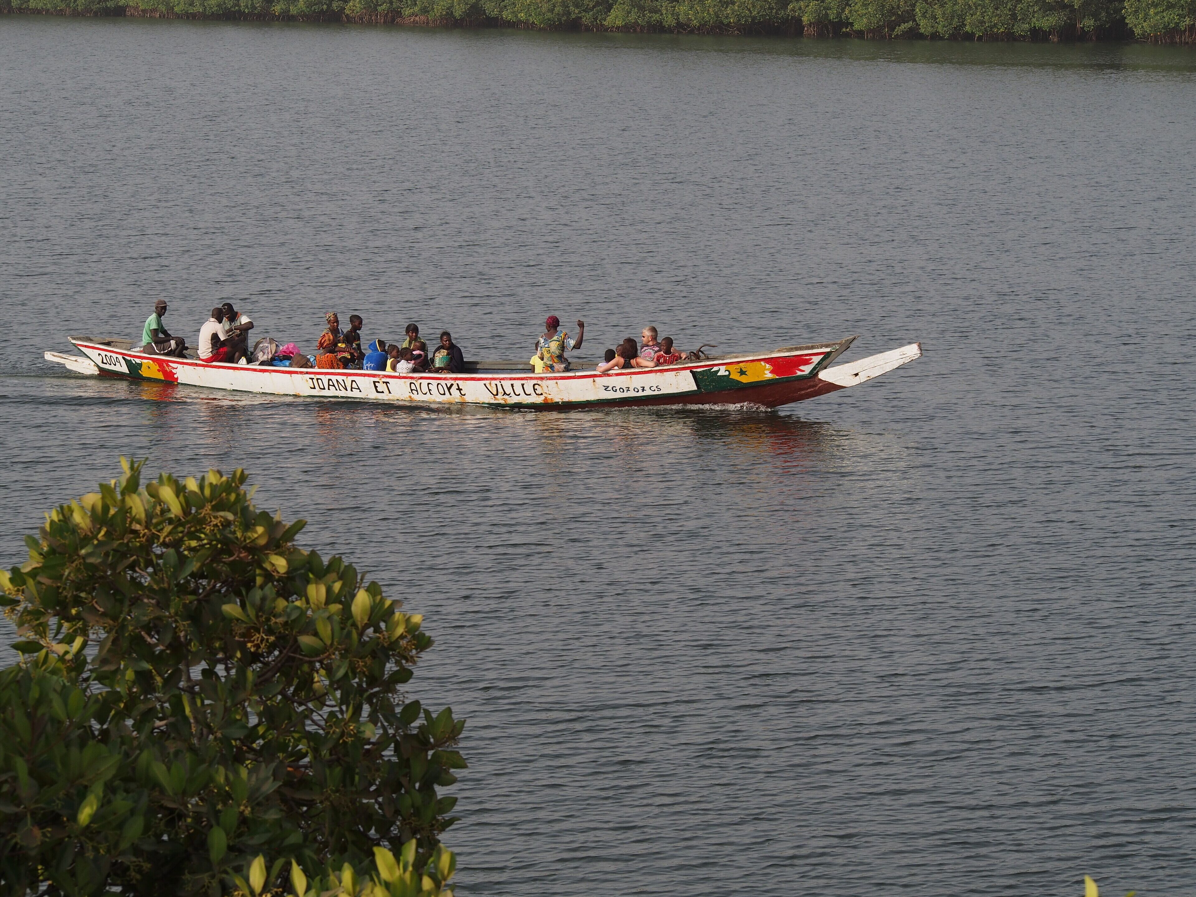 A boat with passengers on a calm body of water, surrounded by greenery.