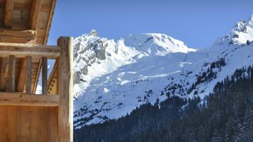 Una cabaña de madera con vistas a montañas nevadas y una ladera boscosa.