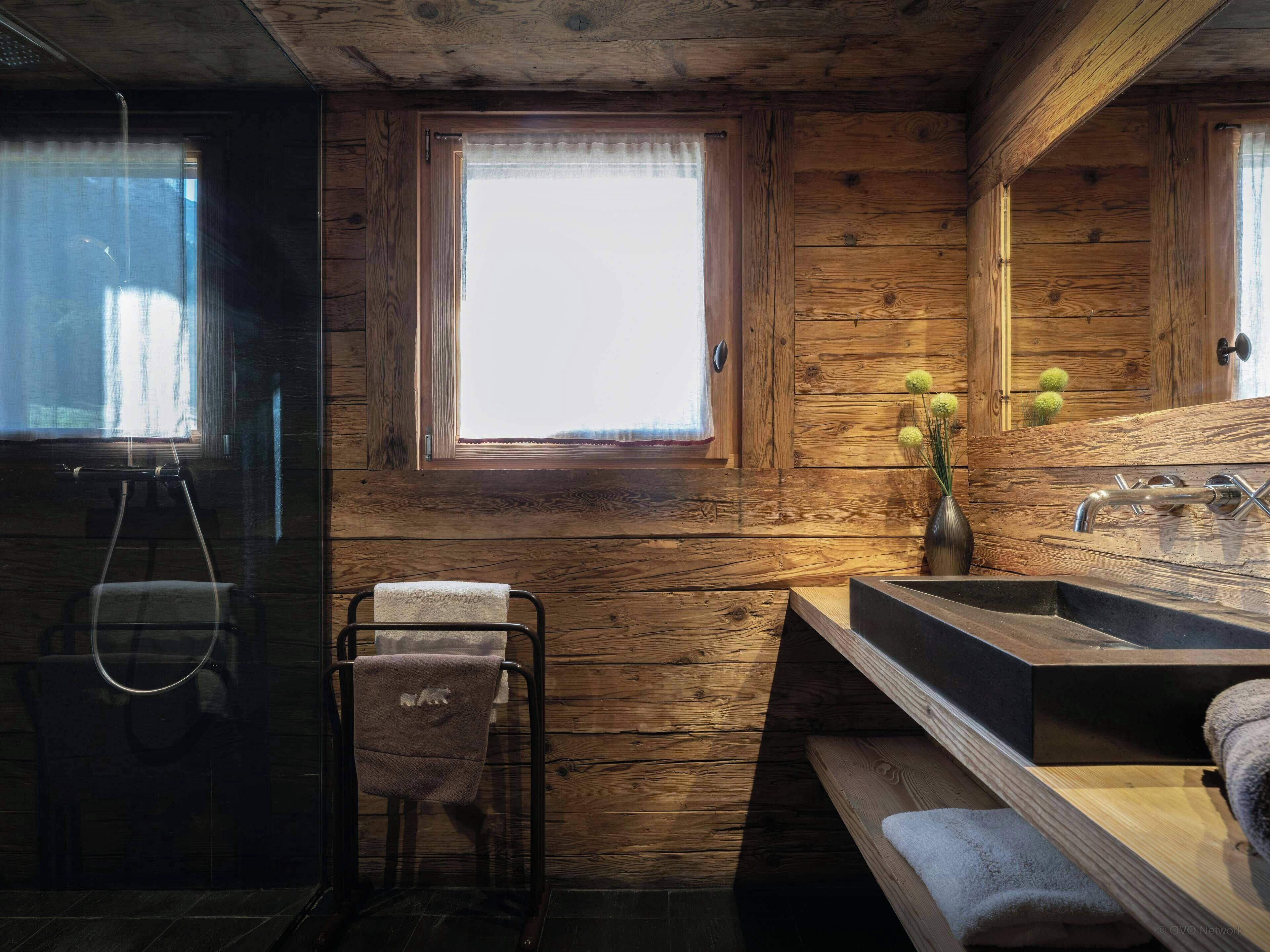 Baño de cabaña de madera con ventana, lavamanos y perchero.