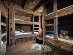 Una cabaña rústica de madera con literas, una ventana y un osito de peluche, y juegos de mesa en el suelo.