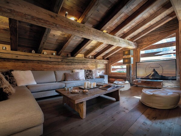 Interior acogedor de una cabaña de troncos con sofá, una mesa de centro de madera y un televisor mostrando Paramount.