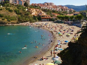 A crowded beach with people swimming and sunbathing, surrounded by buildings and hills.