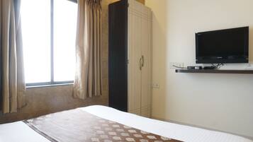 Habitación de hotel con cama, armario, televisor montado en la pared y ventana con cortinas.