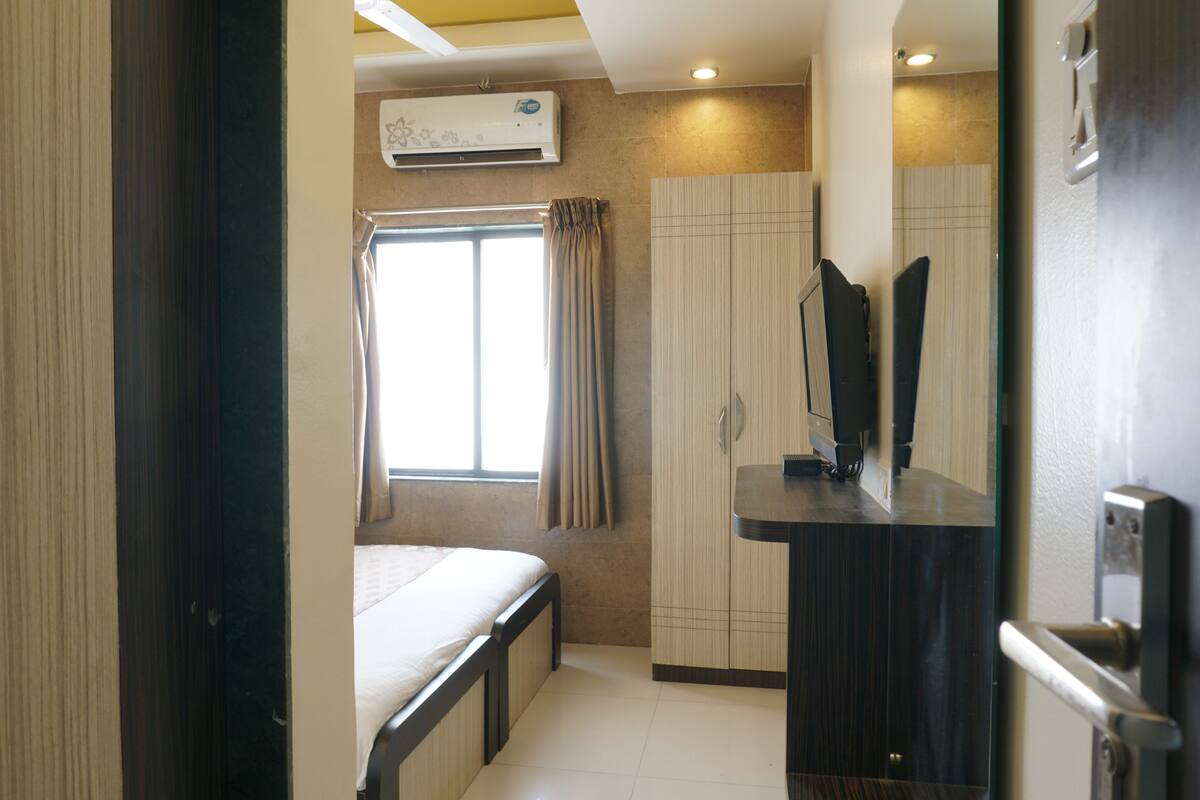 Una habitación de hotel con cama, ventana con cortinas, armario y espejo.