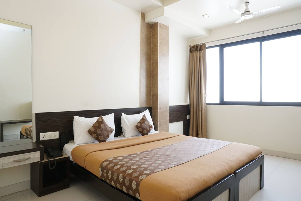 Una habitación de hotel con una cama, una mesita de noche, un espejo y una ventana con cortinas.