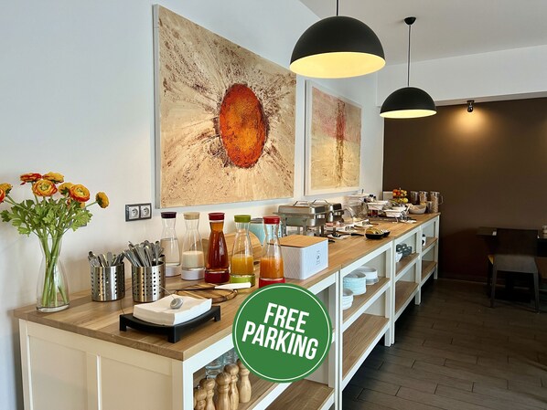 A hotel reception area with a buffet setup, including various food items and condiments, and a sign indicating free parking. -  Grand Petit Hotel (Prague)