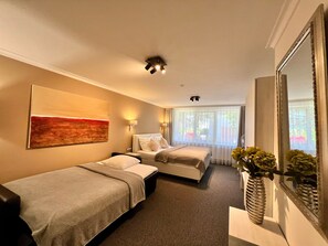 A hotel room with two beds, a large mirror, a painting, and a vase with flowers. -  Grand Petit Hotel (Prague)