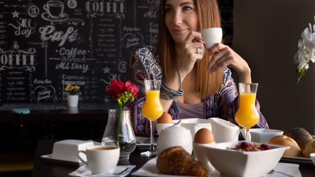 A breakfast setting with a coffee cup, orange juice, eggs, croissants, and a vase of flowers on a table. -  Grand Petit Hotel (Prague)