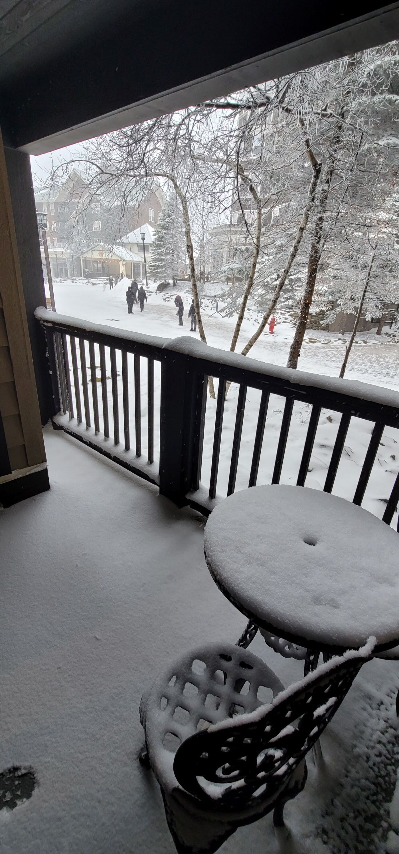 A snow-covered outdoor area with a metal bench and a table, surrounded by a railing.