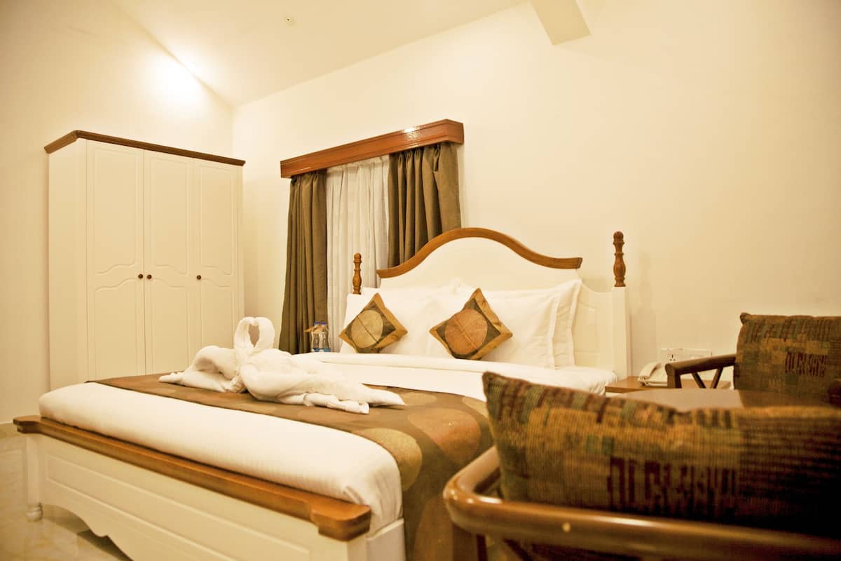 A hotel room with a bed, a chair, a wardrobe, and a window with curtains.