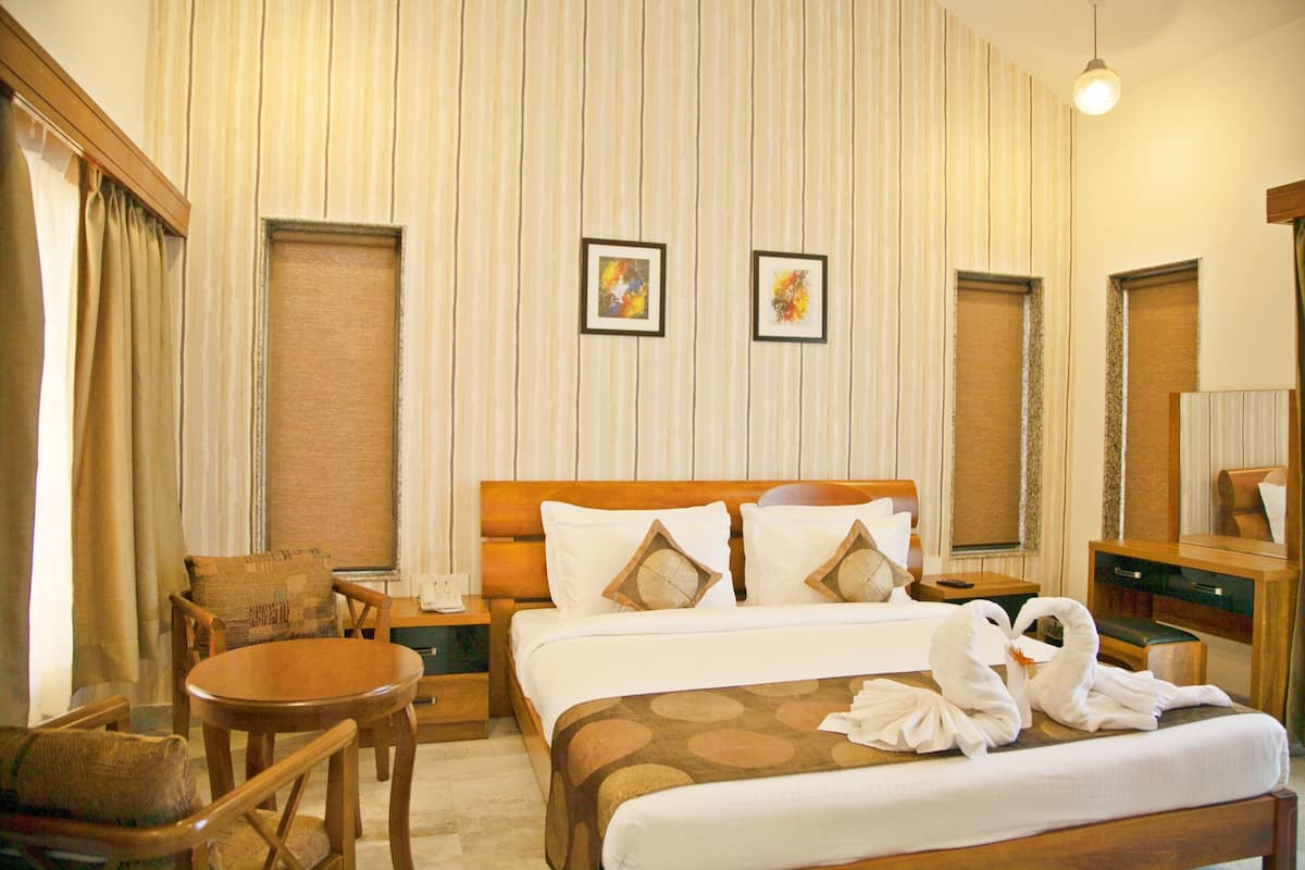 A hotel room with a bed, a wooden chair, a small table, and a nightstand.