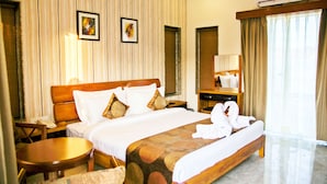 A hotel room with a large bed, a bedside table, a chair, a desk, a mirror, and a window with curtains. - Graces Resort (Sehore)