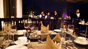 A restaurant table set with wine glasses, plates, and cutlery, with a view of diners in the background. - Graces Resort (Sehore)