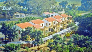 A multi-story hotel with a red-tiled roof, surrounded by lush greenery and a river. - Graces Resort (Sehore)