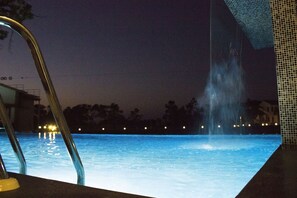 A nighttime pool area with a water feature and a metal ladder.