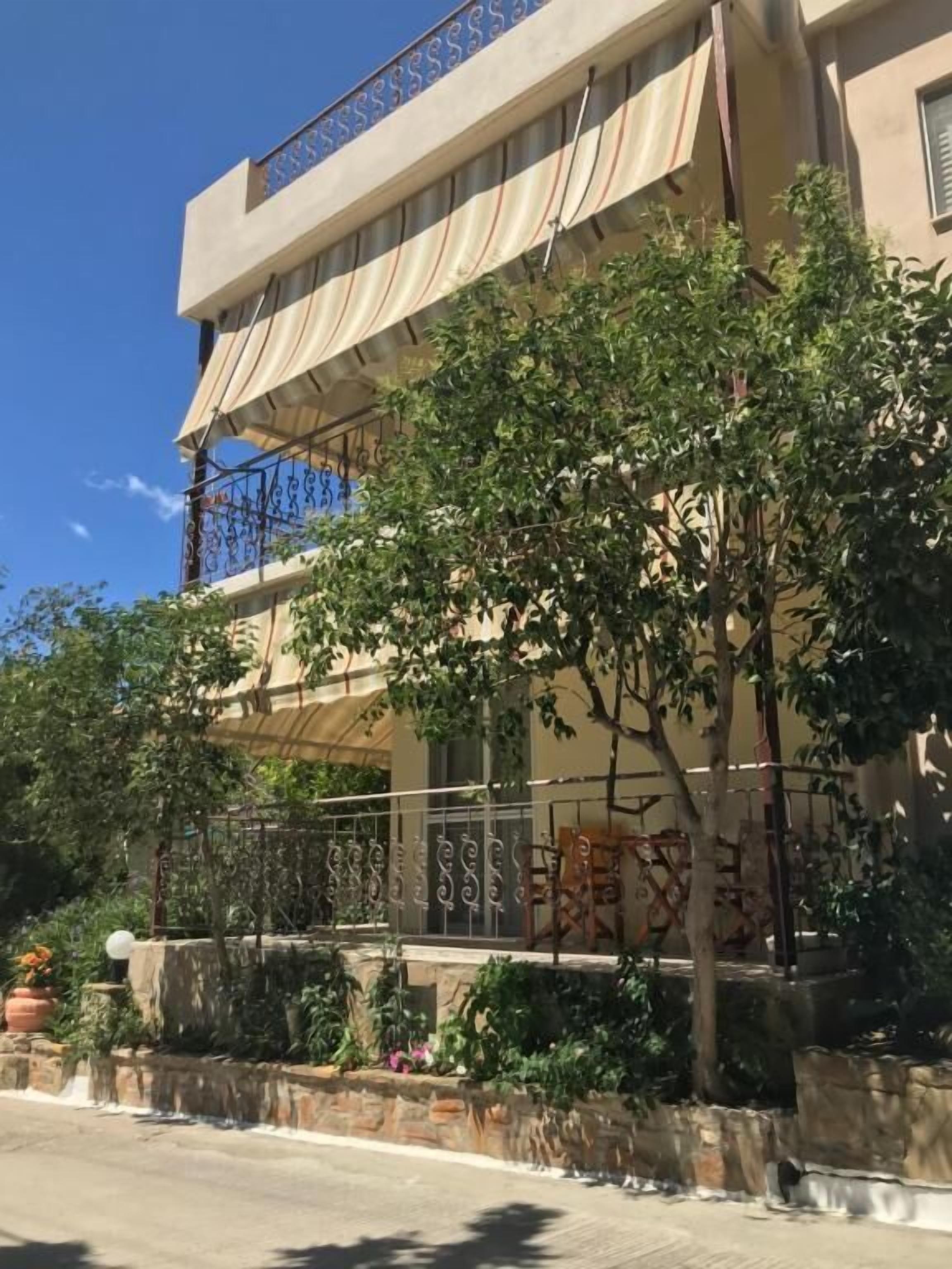Un edificio de dos pisos con un balcón, un muro de piedra y un árbol en primer plano.