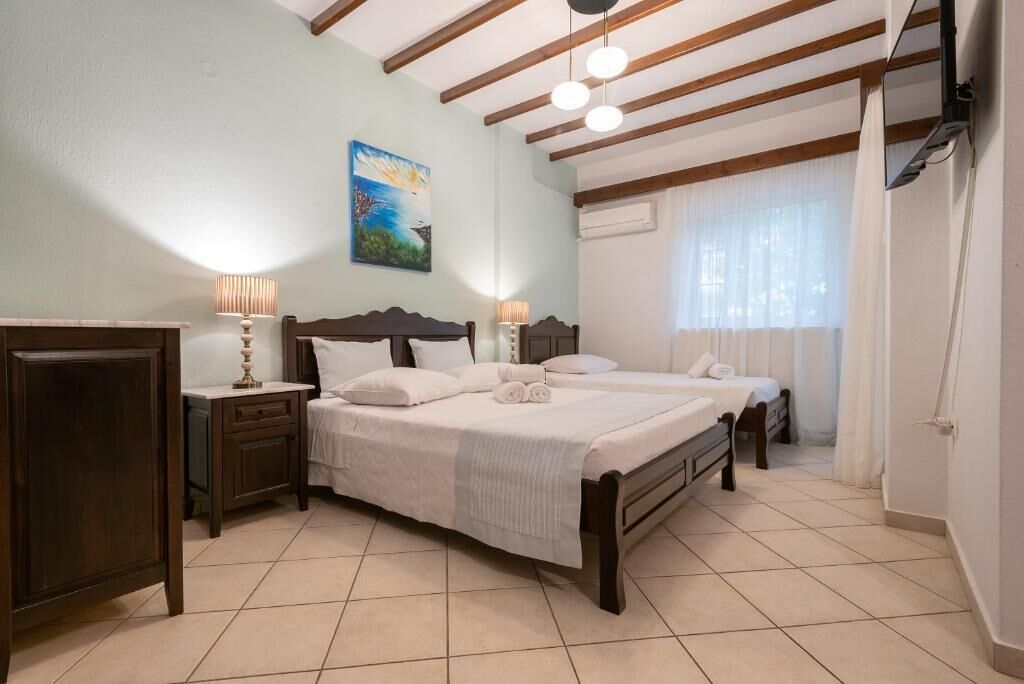 A bedroom with a large bed, two bedside tables, a nightstand, a painting on the wall, and a window with curtains.
