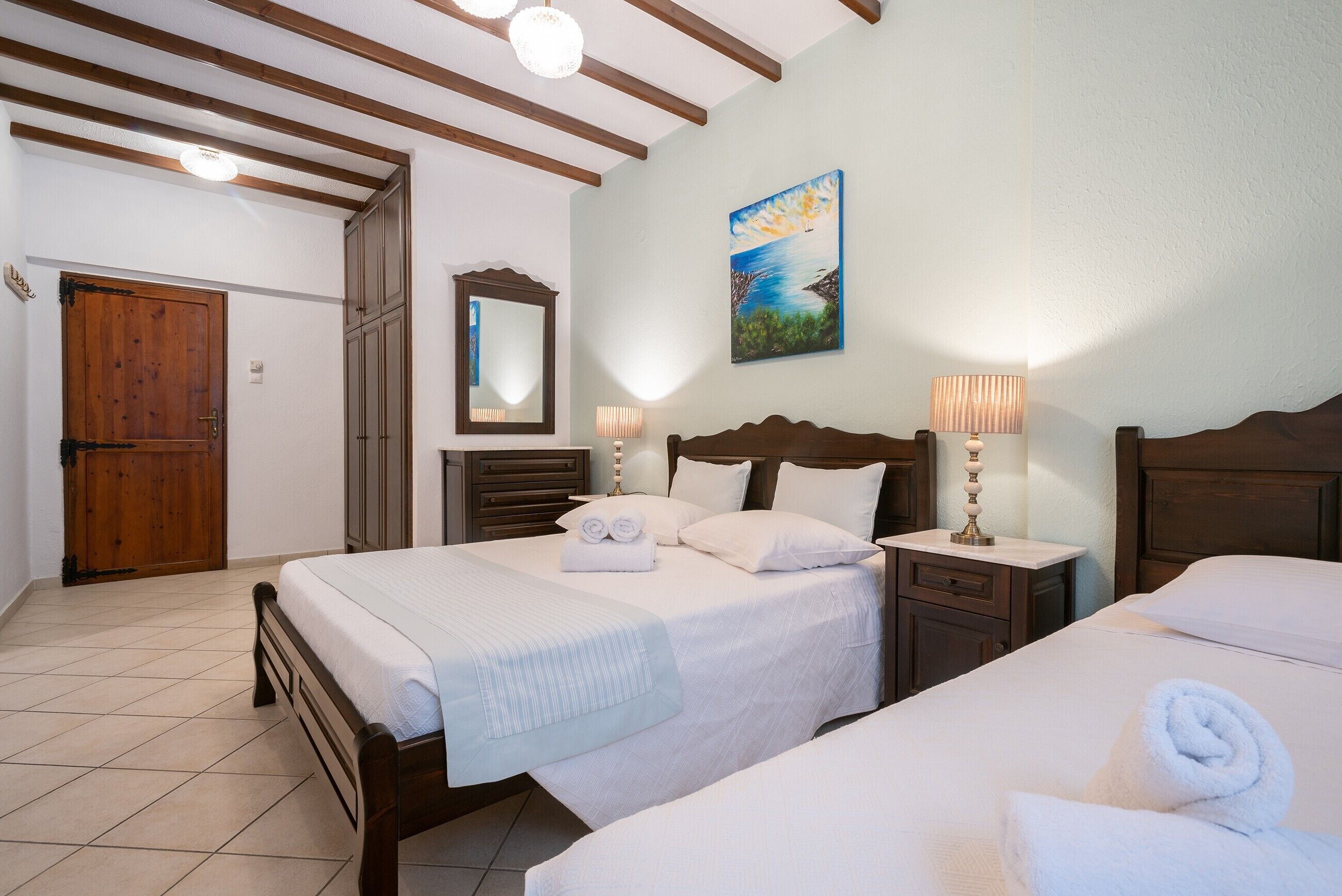 A hotel room with two beds, a wooden door, a painting, and a mirror.