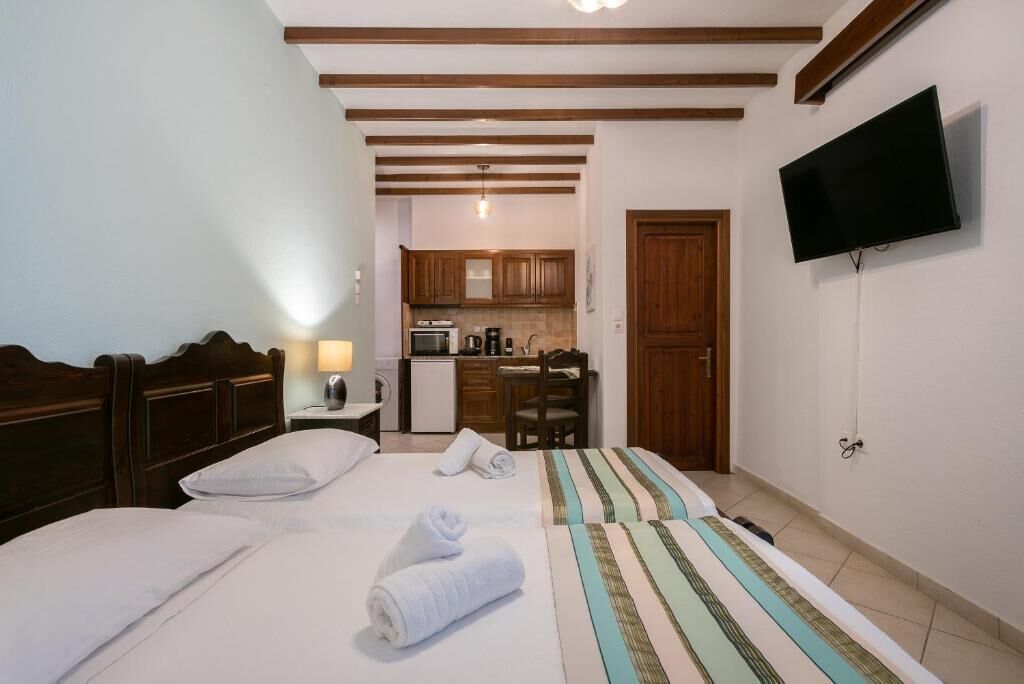 A hotel room with a bed, a TV, a kitchenette, and a wooden ceiling.