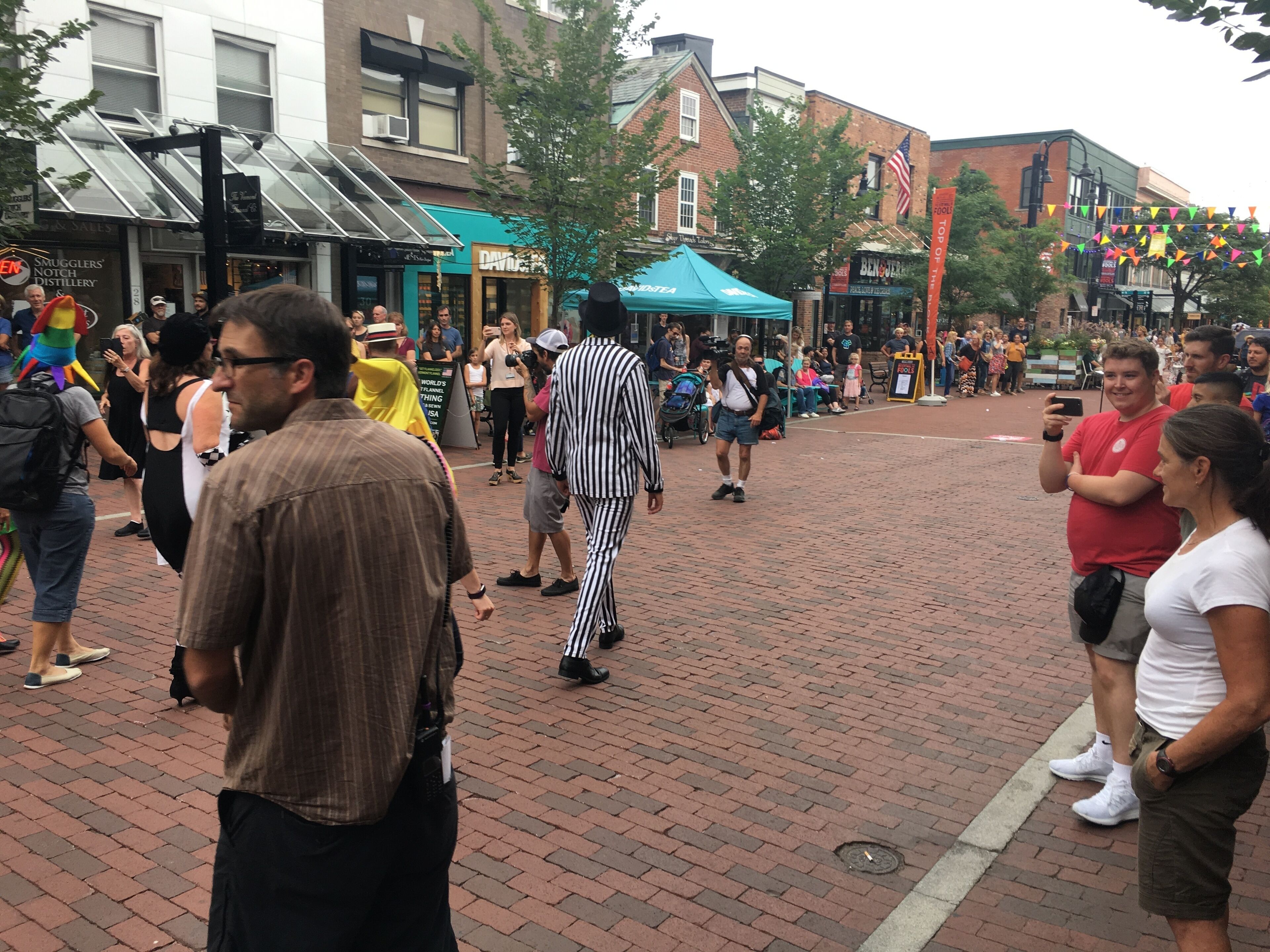 Une place publique avec un sol pavé de briques, des boutiques et des passants.